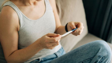 Frau hält lächelnd einen Schwanger&shy;schaftstest in der Hand.