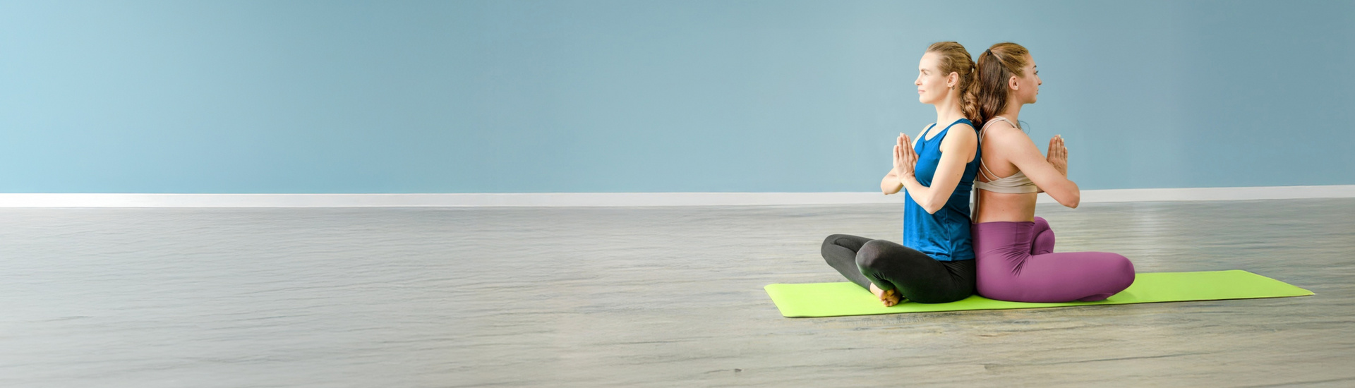 Zwei Frauen sitzen auf einer Yogamatte.