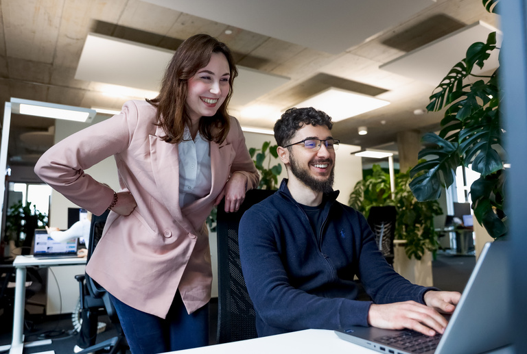 Zwei lächelnde Auszubildende bei der SDK schauen zusammen auf einen Computerbildschirm.