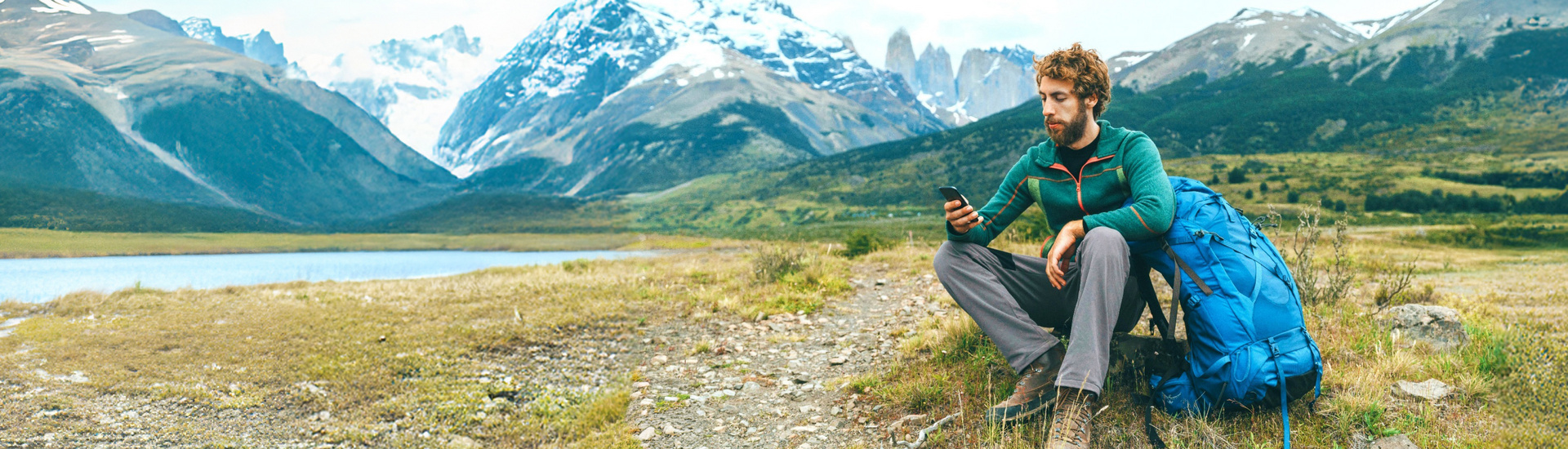 Ein Mann sitzt in der Natur und schaut auf sein Smartphone.
