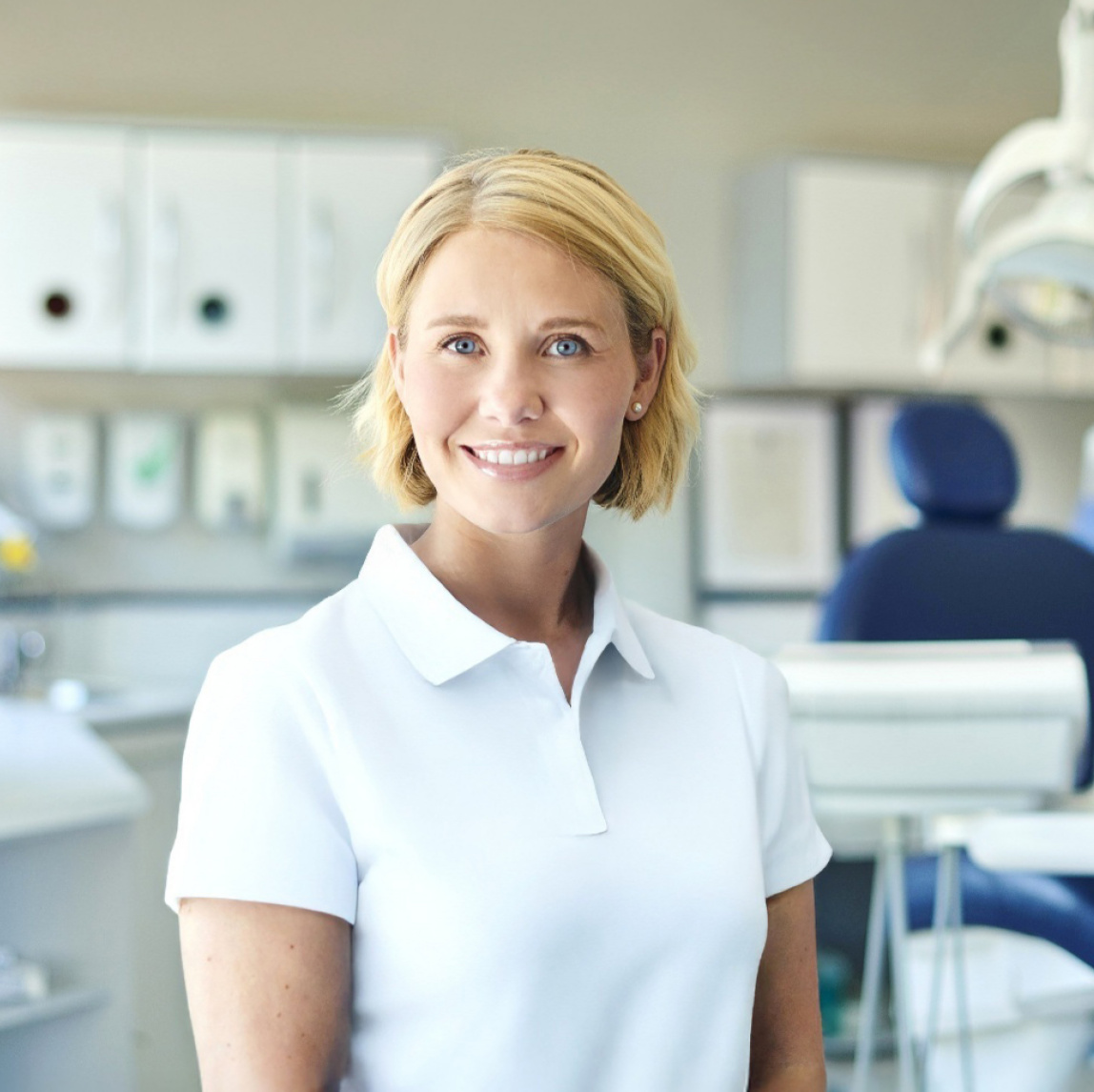 Lächelnde Zahnärztin steht vor einem Zahnarztstuhl.