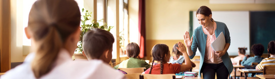 Lehrerin macht einen Handschlag mit einer Schülerin im Klassenzimmer.