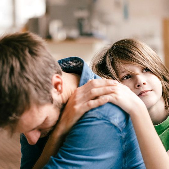 Ein Kind lehnt an einem Mann und sie verschränken ihre Hände.