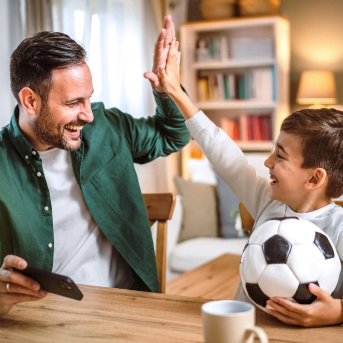 Vater klatscht sich mit seinem Sohn, der einen Fußball hält, ab.