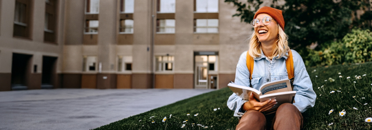 Lächelnde Studentin sitzt vor der Uni.