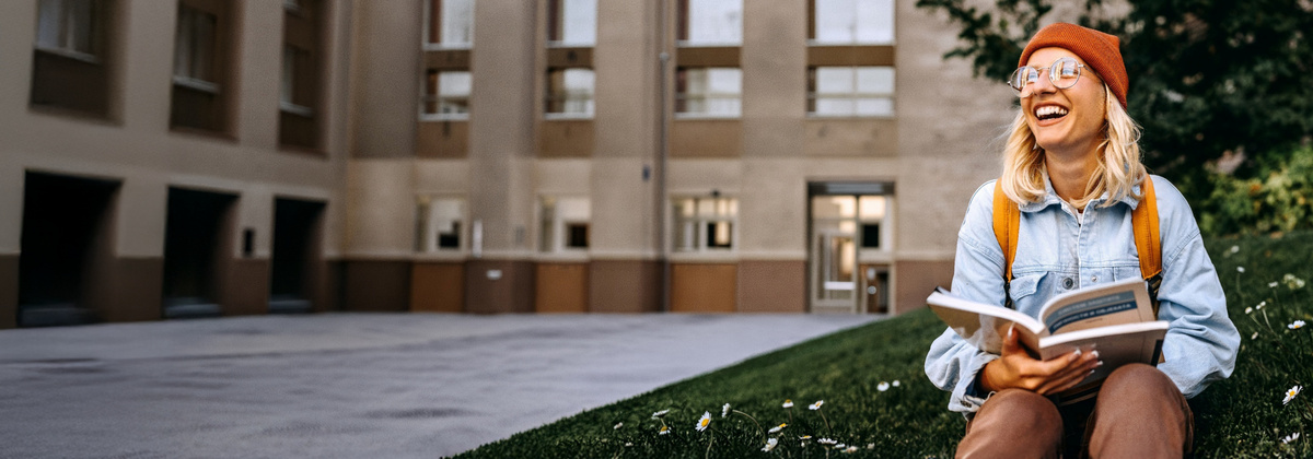 Lächelnde Studentin sitzt vor der Uni.