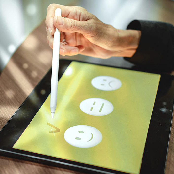 Person macht auf einem Tablet einen Haken bei einem Smiley.