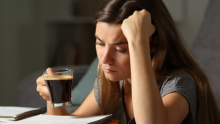 Eine Studentin hängt mit einem frischen Kaffee in der Hand verzweifelt über ihren Lernzetteln.