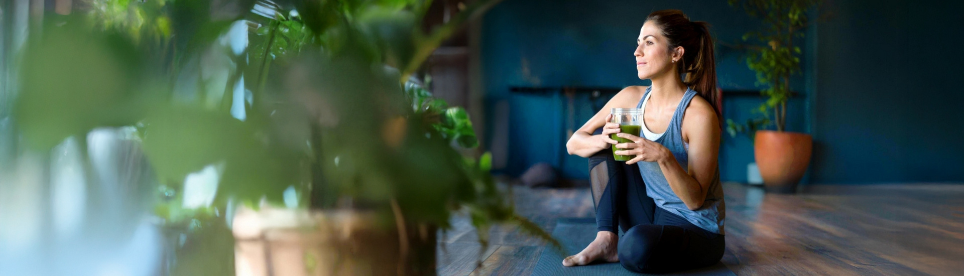 Frau sitzt entspannt mit ihrem Smoothie auf dem Boden.