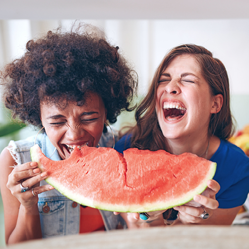 Zwei lachende Personen essen eine Wassermelone.