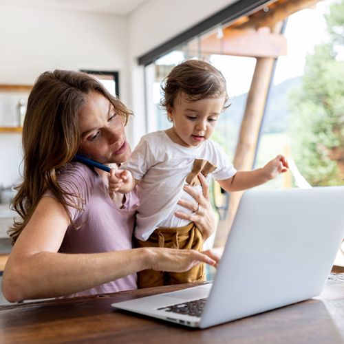 Eine Mutter telefoniert im Homeoffice und hält ihr Kind auf dem Arm.