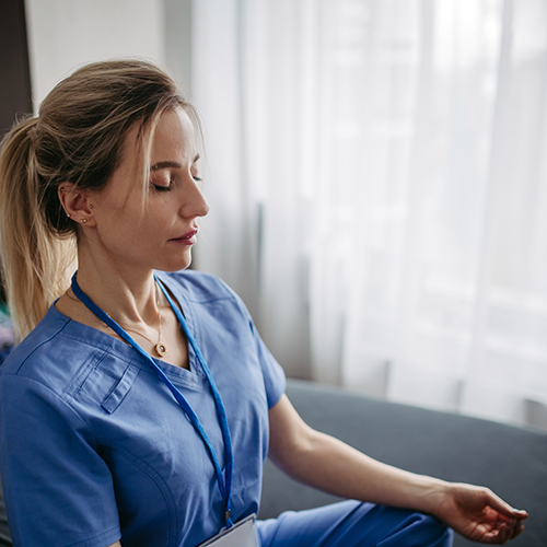 Eine Ärztin sitzt entspannt mit geschlossenen Augen im Schneidersitz und meditiert.